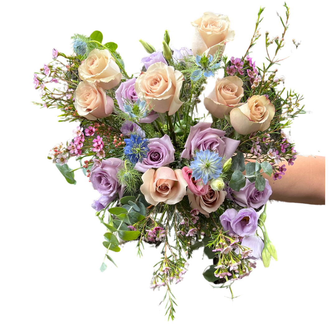 A hand-tied birthday bouquet with a variety of flowers including roses in beige and purple shades, and greenery, wrapped in paper.