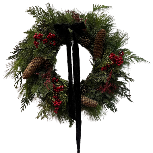 A fresh Signature Wreath made with a grapevine base, cedar, spruce, and red berries, adorned with a black or red  bow and pine cones.