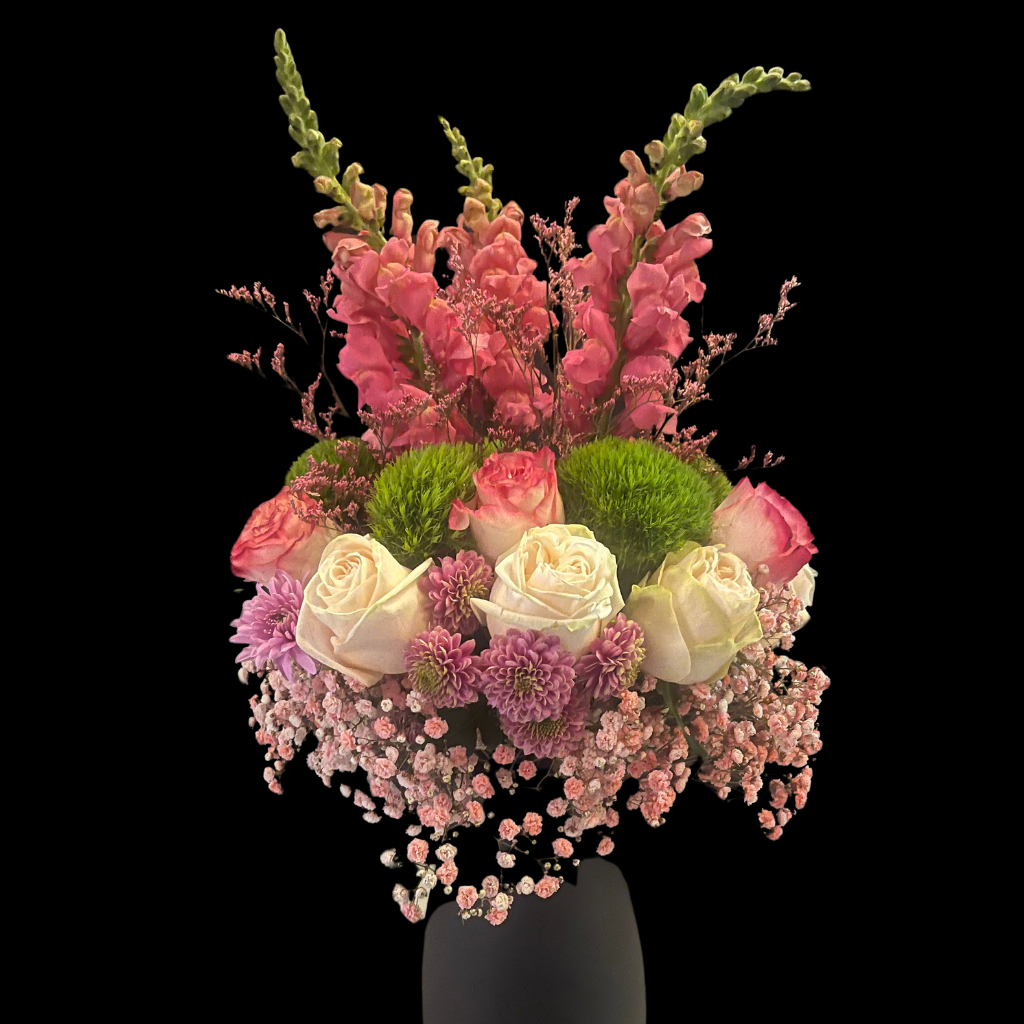 A floral centerpiece arrangement featuring pink and white roses, snap dragons, baby's breath, filler flowers, and green foliage, displayed in a  vase.